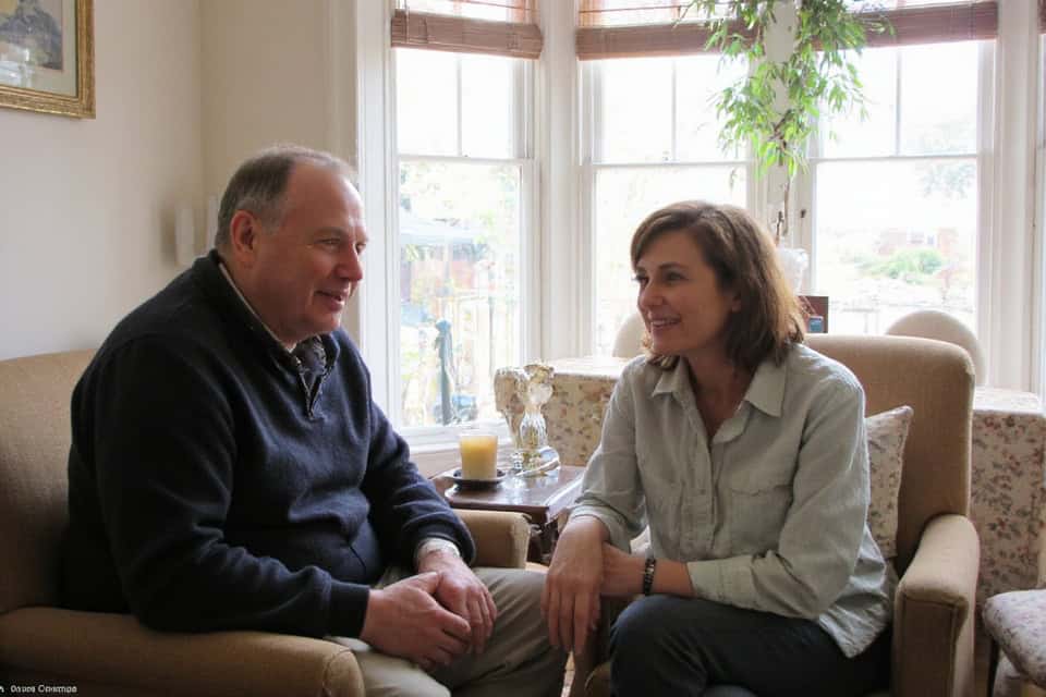 Two People Sitting Comfortably by a Window, Chatting About UK Equity Release Companies in a Bright, Inviting Lounge with Plants.